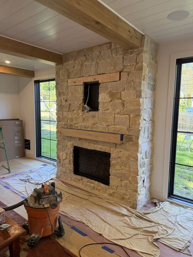 Great room with a stacked-stone fireplace and timber beams, in progress, RDH Construction